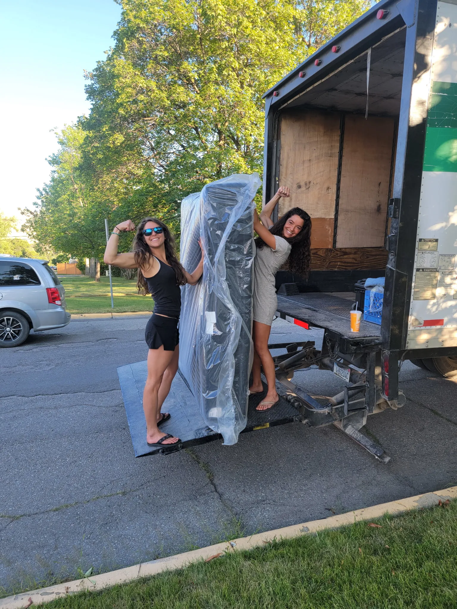 Two Moving On Up crew members loading a shrink-wrapped mattress onto the truck liftgate