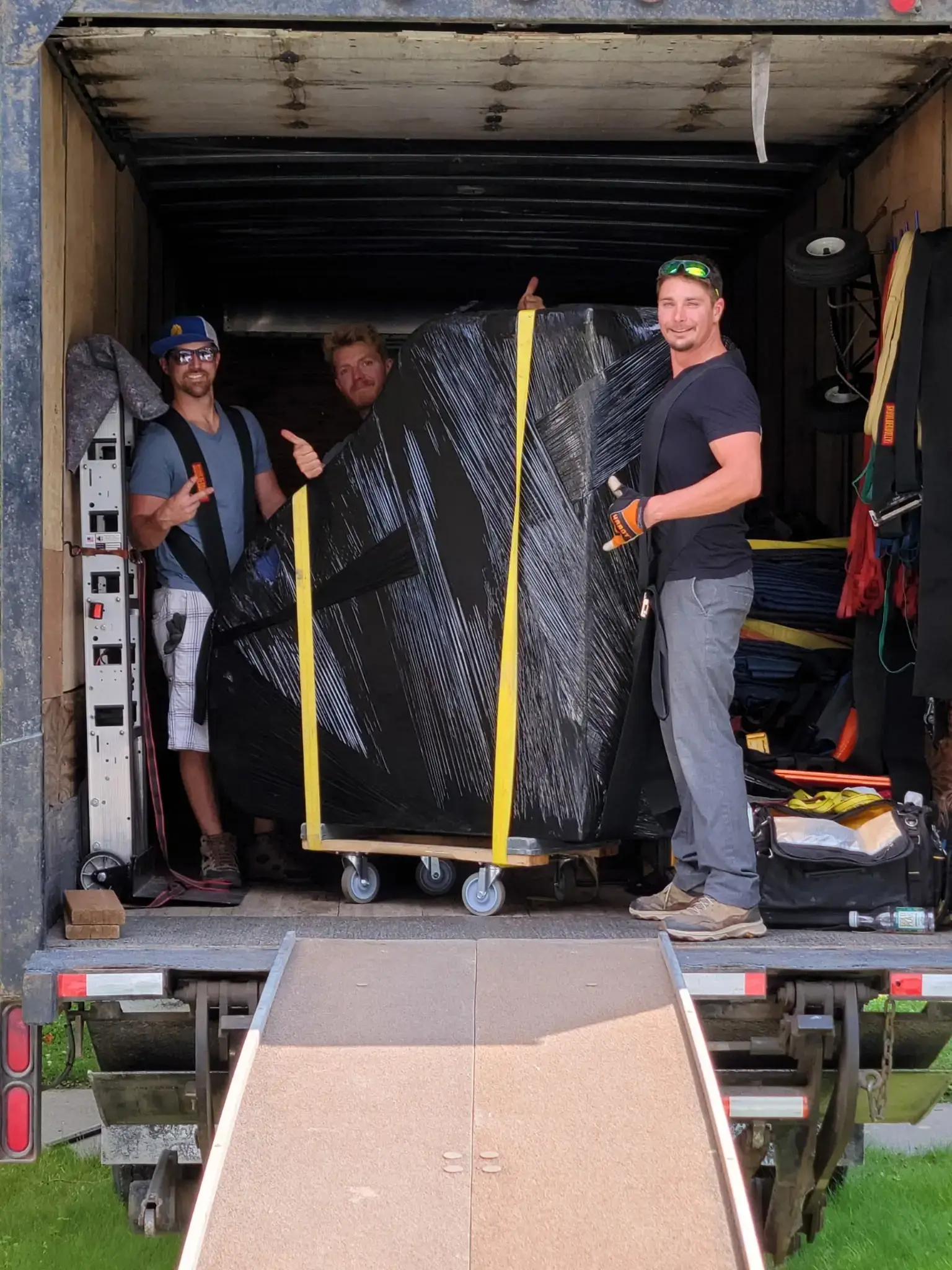 Three Moving On Up crew members giving a thumbs-up around a wrapped piece inside the loaded moving truck