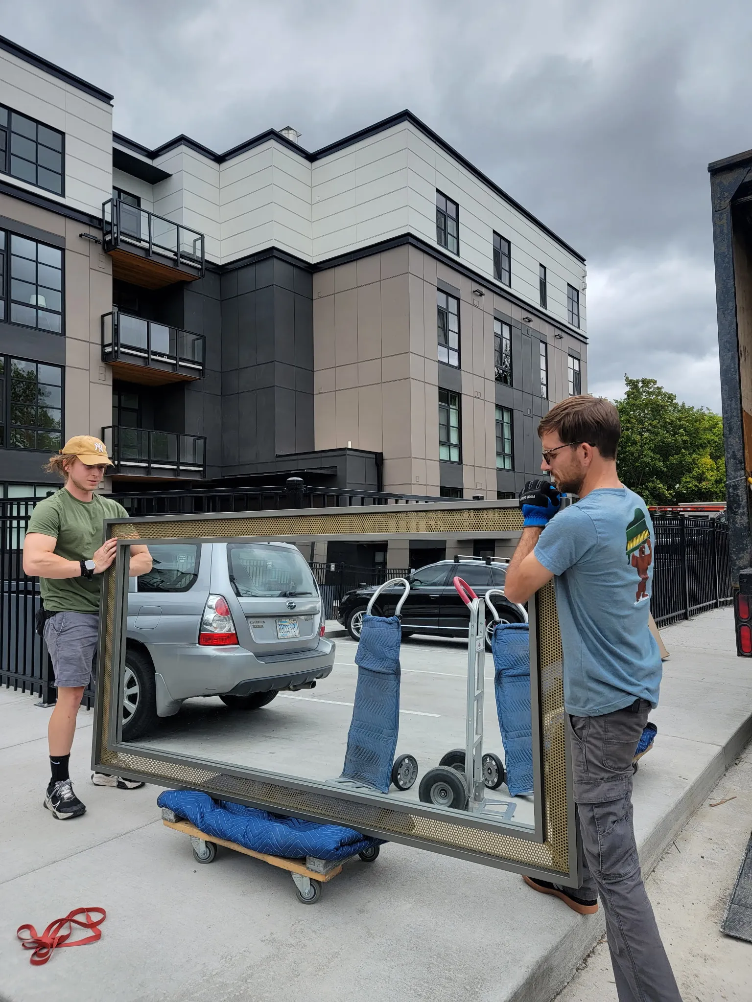 Crew carrying a large framed mirror on a dolly outside an apartment building