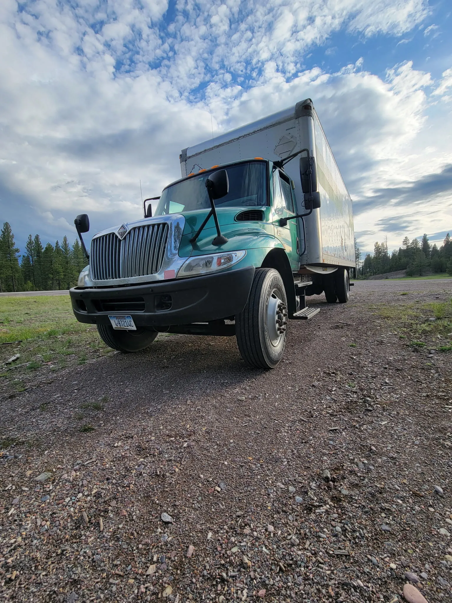 The Moving On Up green box truck parked on a gravel lot under a dramatic Montana sky