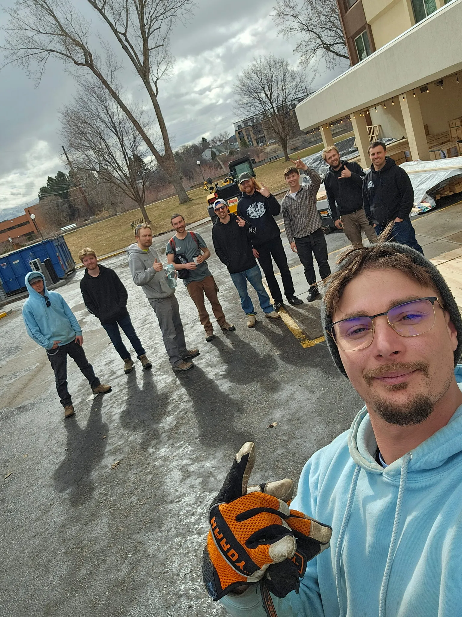 The Moving On Up crew together in a parking lot, several giving a thumbs-up, with a team member taking the selfie up front